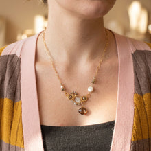Load image into Gallery viewer, A gold chain necklace with a central cluster of white pearls, small gold beads, and a faceted amber-brown pendant, shown worn on a person's neck over a pink cardigan.