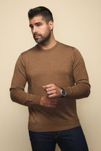 Load image into Gallery viewer, A man wearing a brown long-sleeve crewneck sweater and dark blue jeans, standing against a light tan wall.