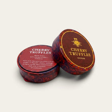 Load image into Gallery viewer, Two round metal tins of cherry truffles on a light beige background. One tin is upright showing the label with the brand name 'CHERRY TRUFFLES' and a crest, while the other lies on its side showing the decorative patterned lid.