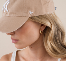 Load image into Gallery viewer, Woman wearing a beige cap with a logo, gold hoop earrings, and a white top on a beige background