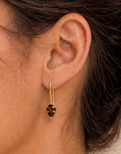 Load image into Gallery viewer, A close-up of a person's ear wearing a gold huggie hoop earring with a dangling pear-cut brown gemstone.